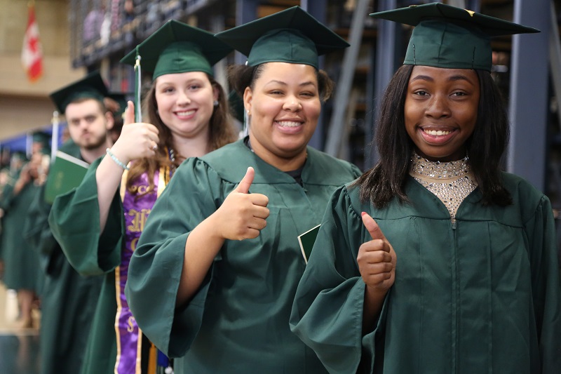 students giving thumbs up in caps and gowns at commencement