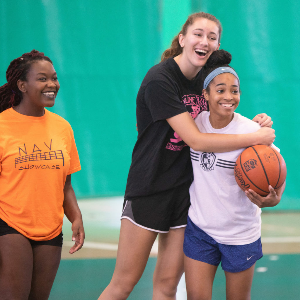 three women's basketball players smiling with two hugging