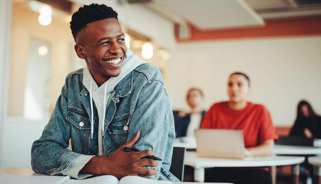Male student sitting in university classroom looking away and smiling