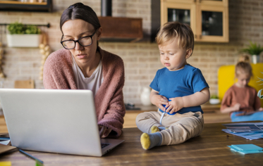 woman looking at laptop with child sitting on counter next to her
