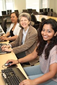 three people sitting in front of computers and smiling